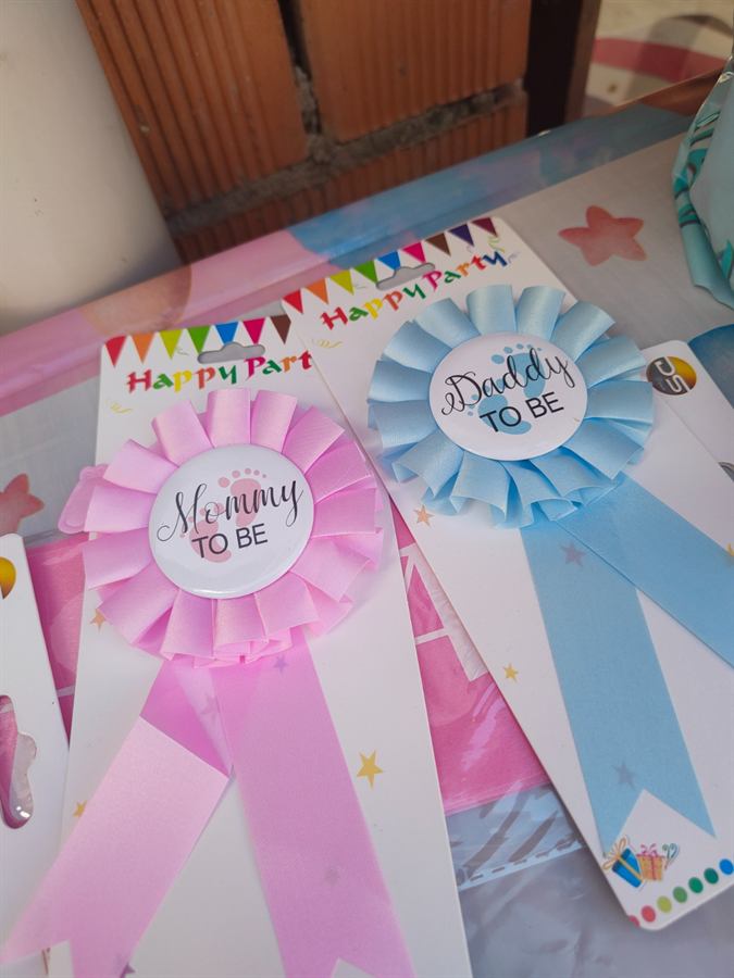 Due coccarde di carta con le scritte Mommy to be e Daddy to be, rosa e azzurra