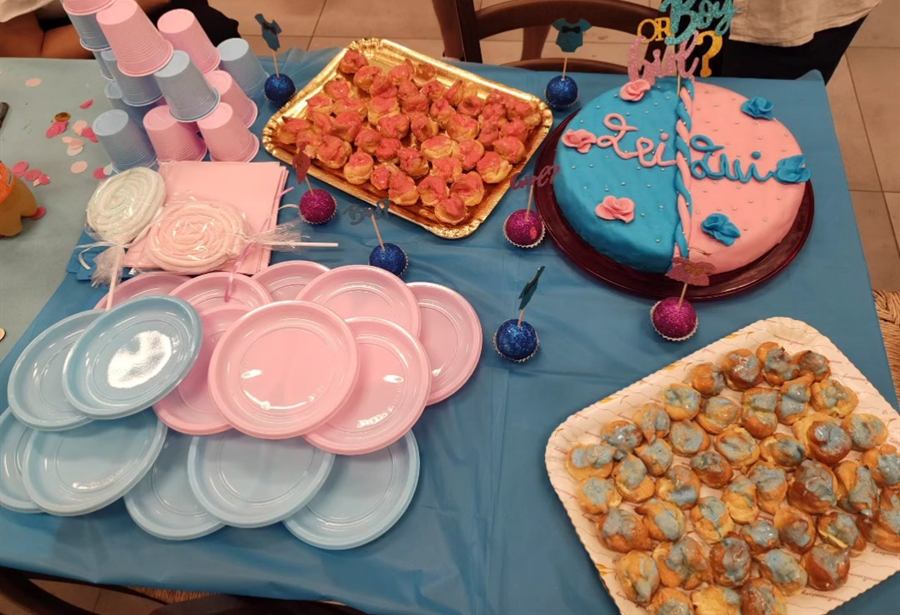 Tavola con piatti rosa e azzurri, vassoi di bignè e torta divisa a metà nei due colori