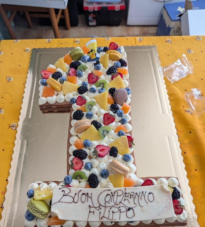Torta a forma di numero uno decorata con frutta fresca, macaron e panna